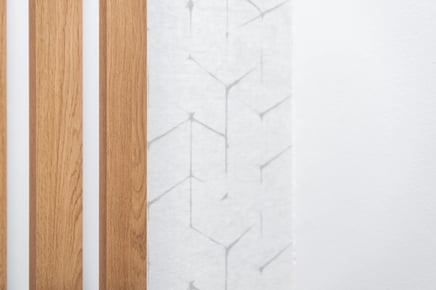 Dřevěné lamely na stěně a tapeta geometrický vzor v interiéru.